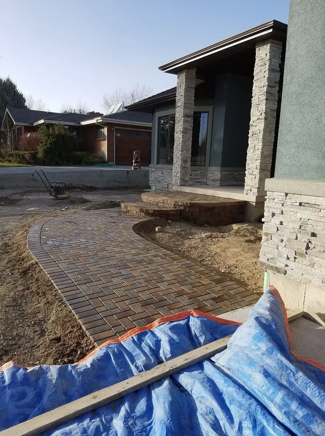 Curved herringbone paver walkway with a rounded paver step leading to a modern home with stacked-stone columns.