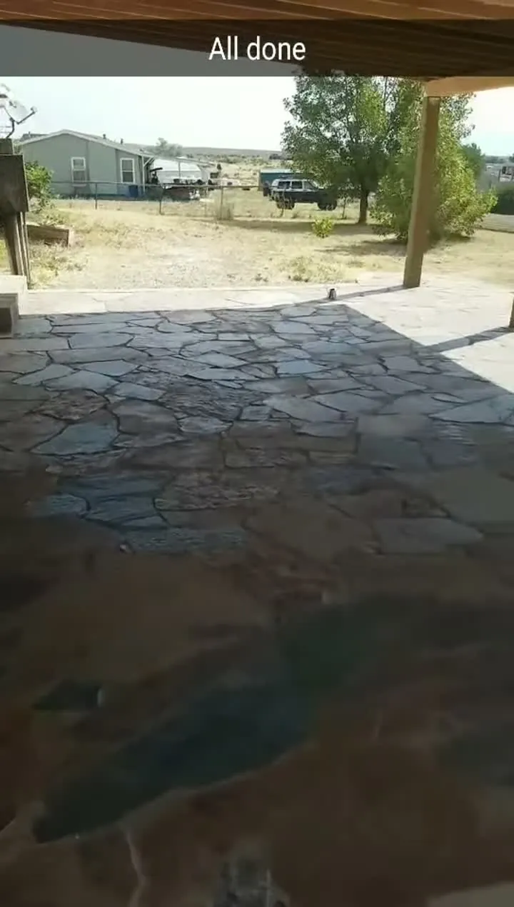 Large flagstone patio under a covered deck extending to a round fire pit with a curved seat wall and block pillars.