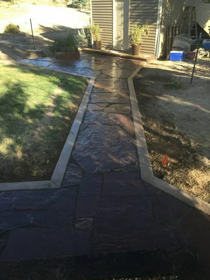 Flagstone walkway in purple-brown stone bordered by concrete edging, leading to a shed door.