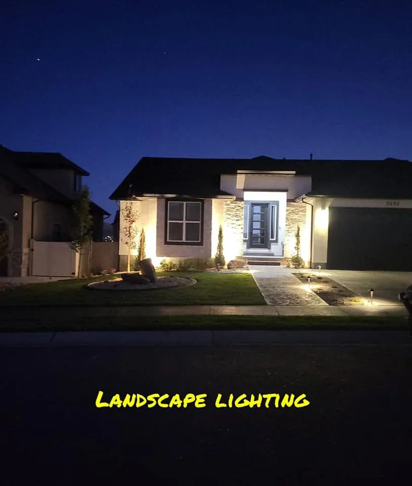 Front yard at dusk with uplighting on stone columns and path lights along a stamped walkway and planting bed.