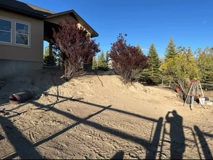 Graded bare dirt yard beside a house with a survey tripod, before sandstone steps were set.