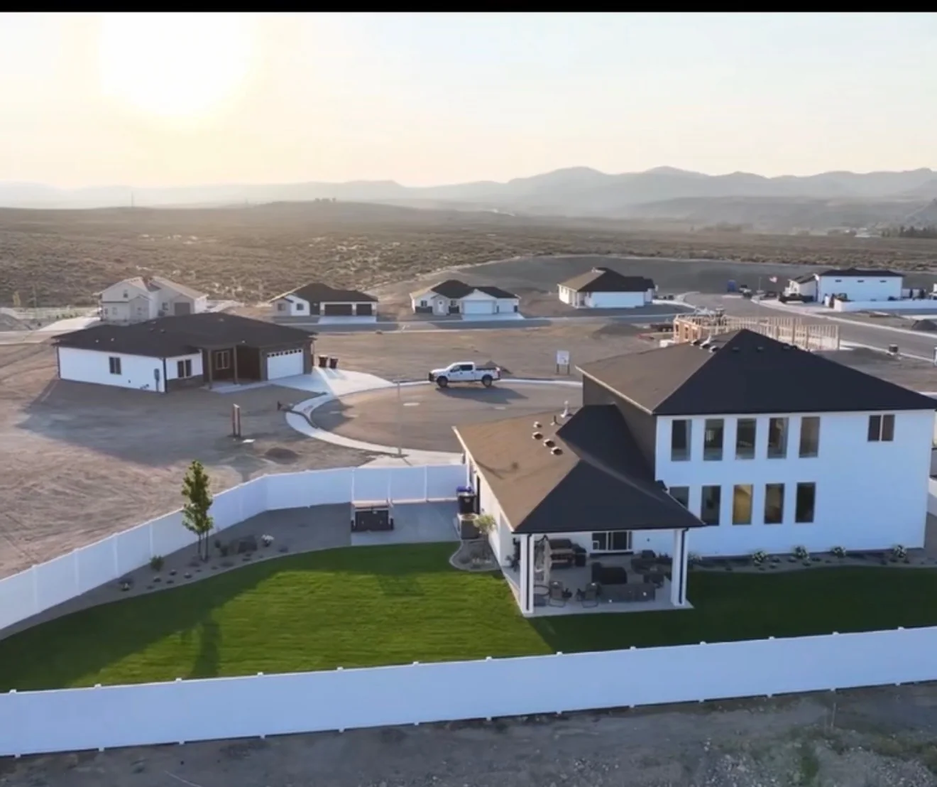 Aerial view of a fenced backyard lawn and house with neighboring properties beyond.