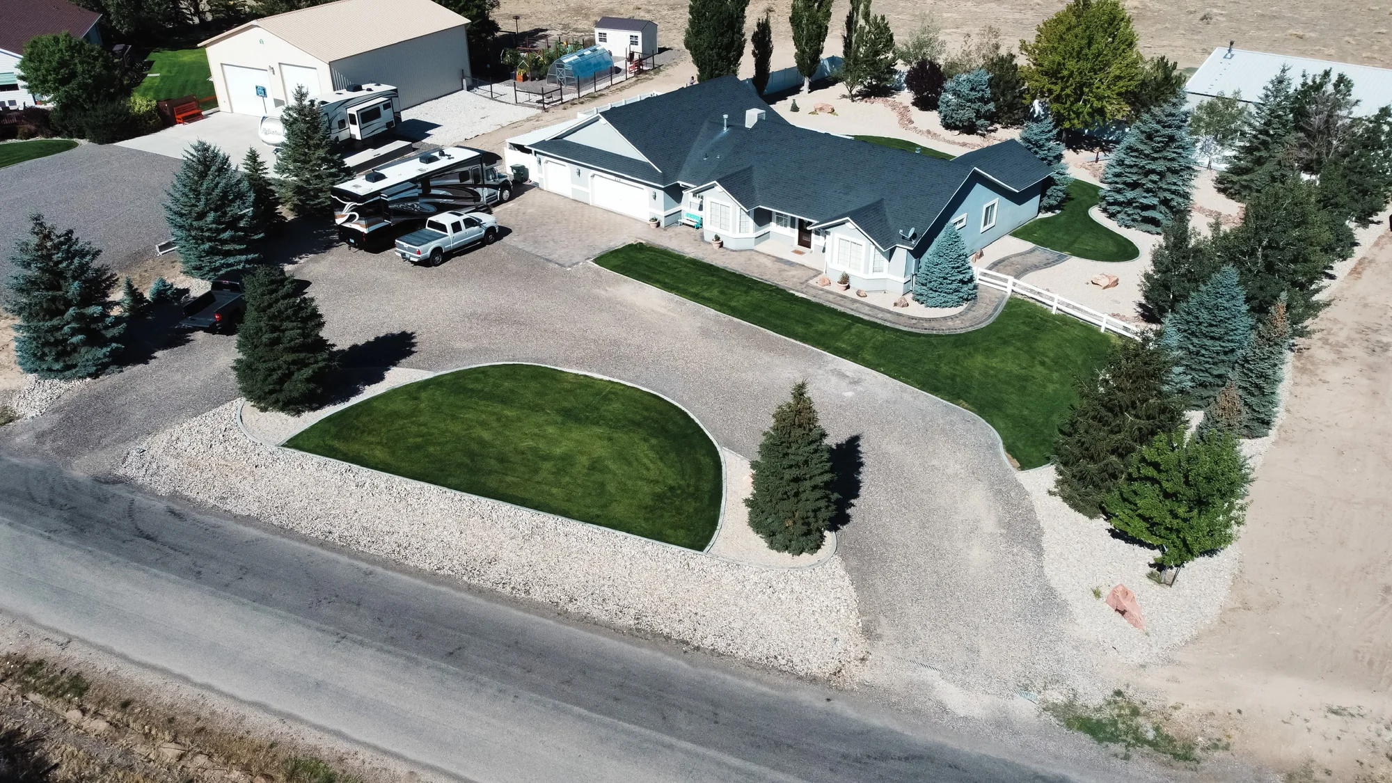 Aerial view of a front lawn island with trees, a broad driveway and rock-covered beds.