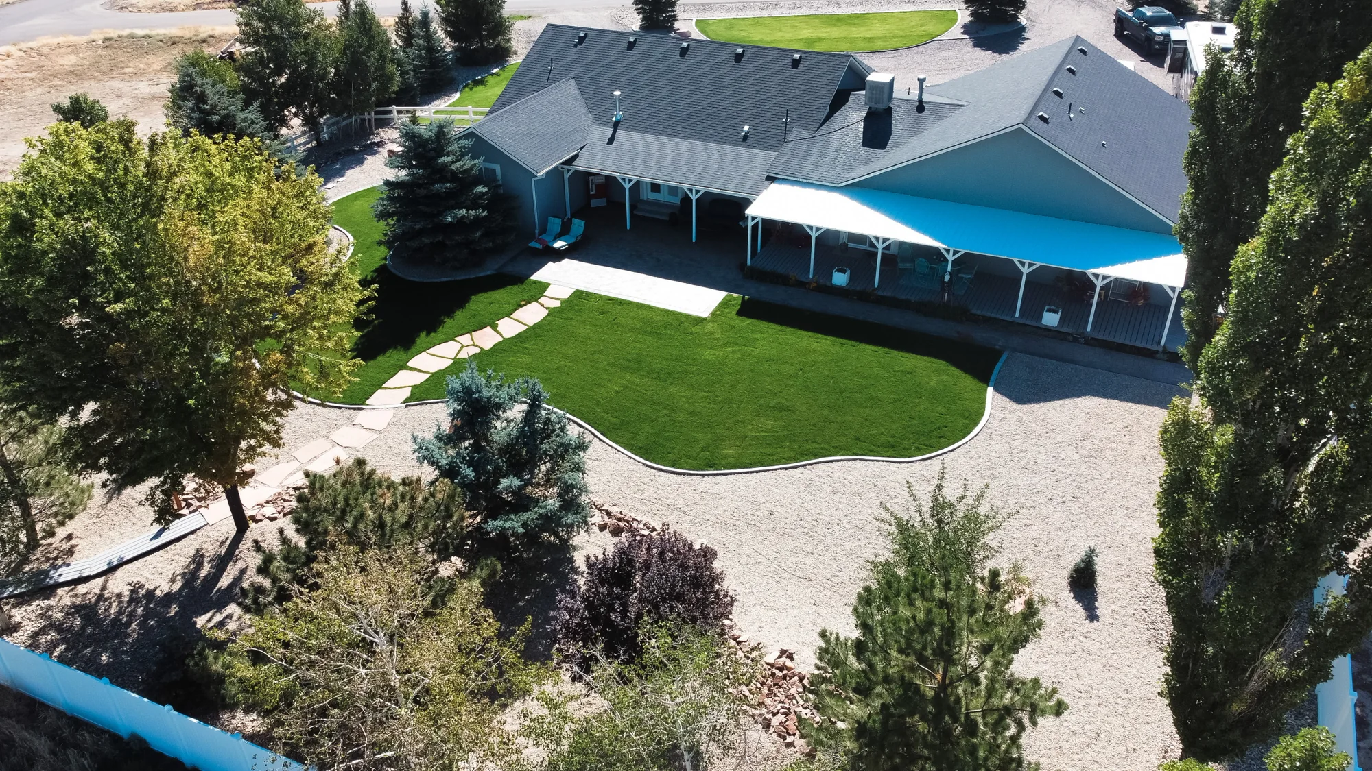Aerial view across a lawn with curved pale borders, trees and planted beds beside a house.