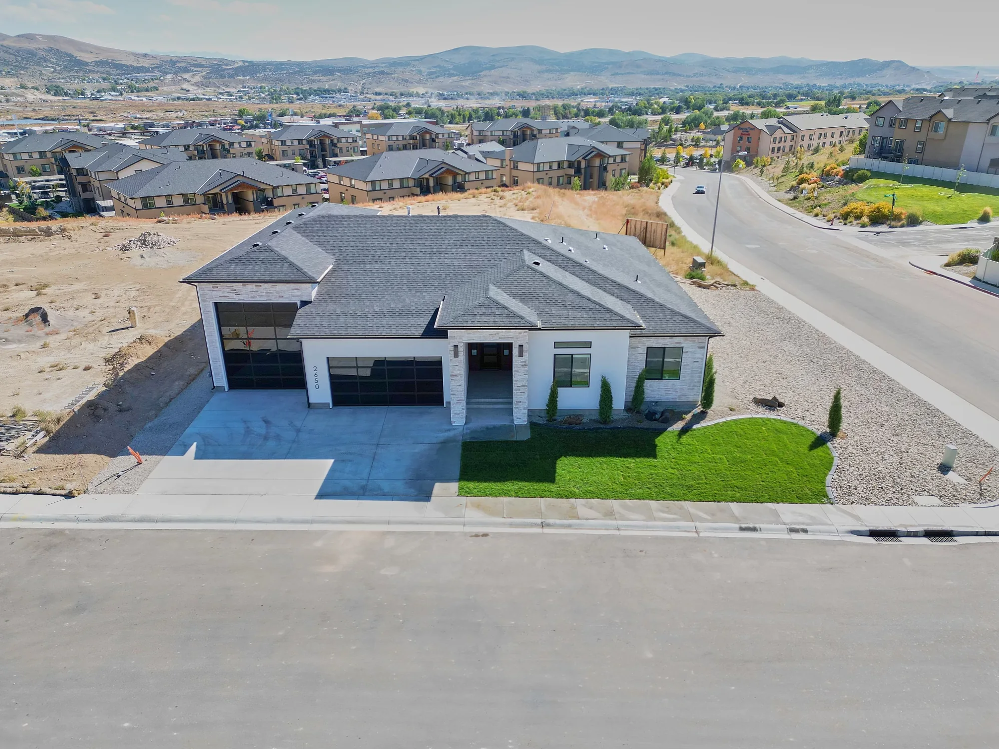 Aerial view of a newly landscaped front lawn and driveway beside a house with surrounding bare ground.