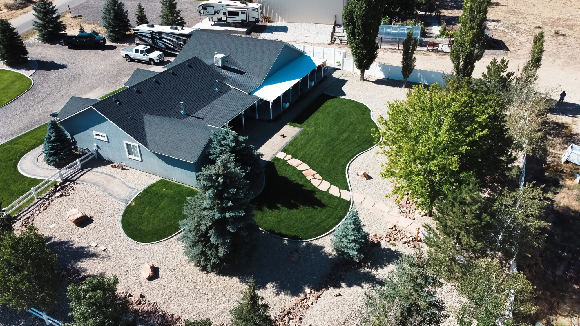 Aerial view of a landscaped yard with green lawn, curved borders, trees and rock-covered beds.
