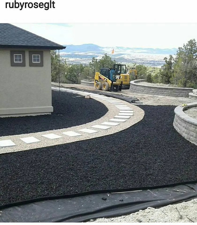 Curving path of square concrete pavers in light gravel between beds of black rock beside a tan stucco building.
