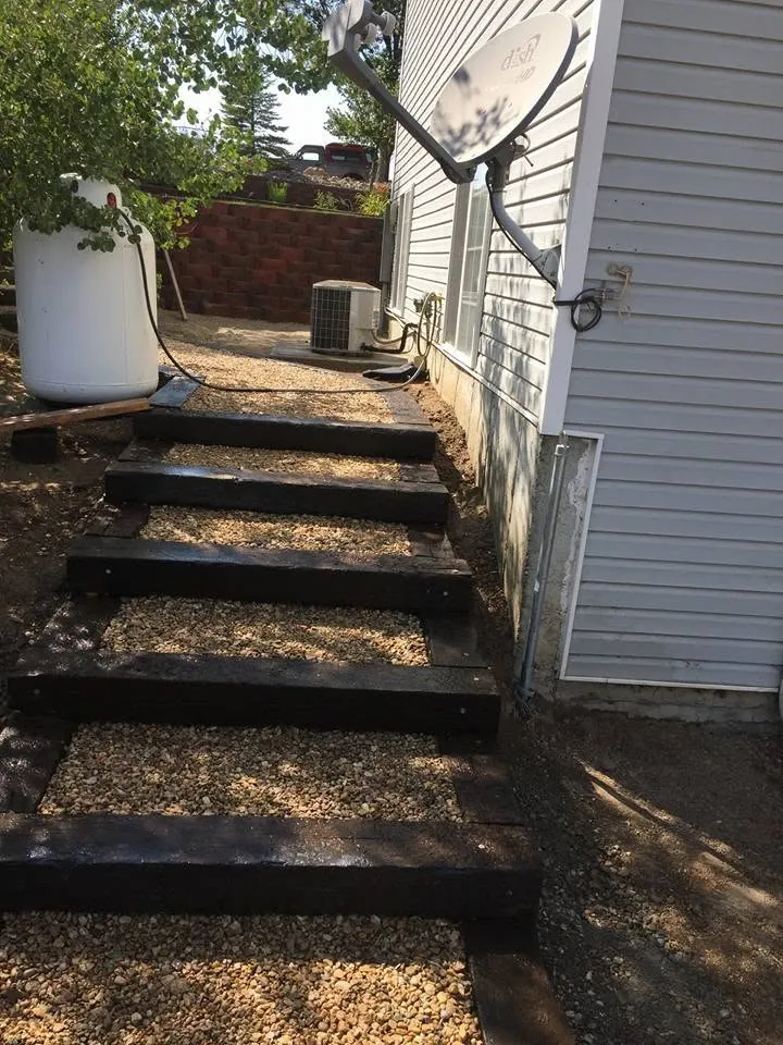 Side-yard staircase of dark timber risers and pea gravel treads beside a white-sided house.